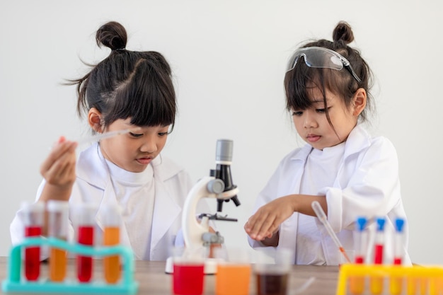 Education, science, chemistry and children concept - kids or students with test tube making experiment at school laboratory