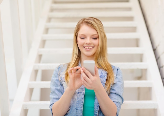 концепция образования и технологий - улыбающаяся студентка со смартфоном, сидящая на лестнице