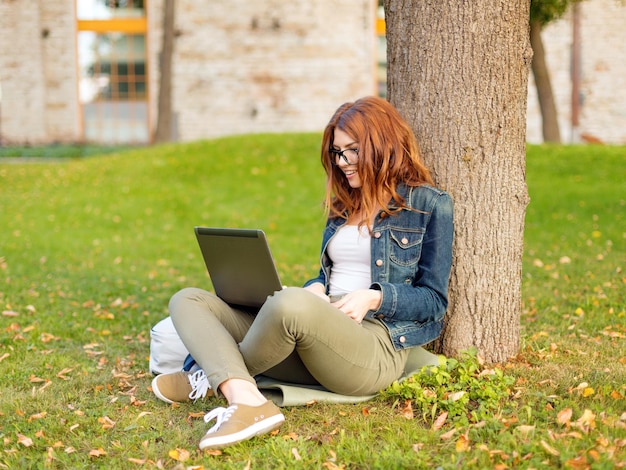 교육, 기술 및 인터넷 개념 - 노트북 컴퓨터가 있는 안경을 쓰고 웃고 있는 빨간 머리 십대