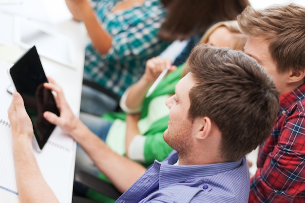 Photo education, technology and internet concept - smiling students looking at tablet pc at school