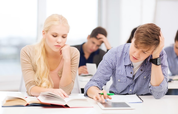 education, technology and internet concept - tired students with tablet pc, books and notebooks preparing for exam