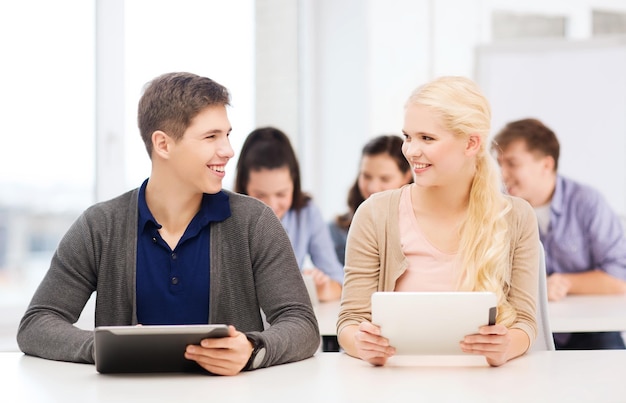 education, technology and internet - two smiling students looking at tablet pc in lecture at school