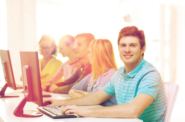 education, technology and school concept - smiling male student with classmates in computer class