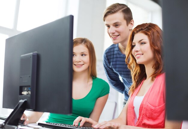 education, technology, school and people concept - group of smiling students having discussion in computer class at school