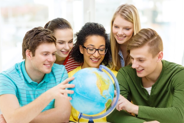 Concetto di educazione, viaggi e geografia - cinque studenti sorridenti guardando il globo terrestre a scuola