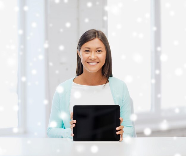 education, winter, technology and people concept - smiling young woman showing blak blank tablet pc computer screen indoors