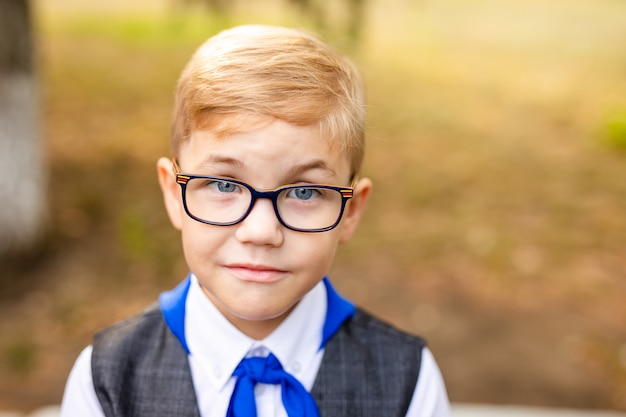 Tema educativo: ritratto di uno scolaro con grandi occhiali neri e cravatta blu. cortile della scuola, inizio delle lezioni