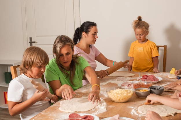 Gli educatori insieme ai bambini in età prescolare fanno la pizza