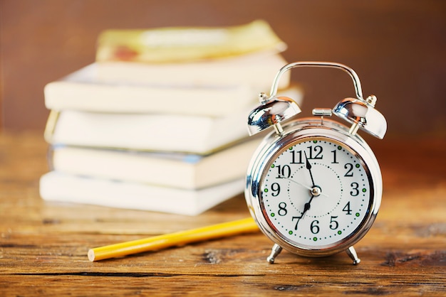 Photo eduction concept. alarm clock and books on wooden table, selective focus