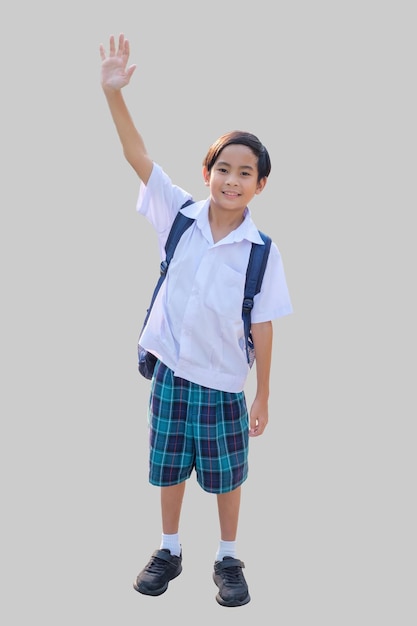Een 10-jarige Aziatische jongen in een schooluniform staat met zijn handen omhoog en zwaait en glimlacht