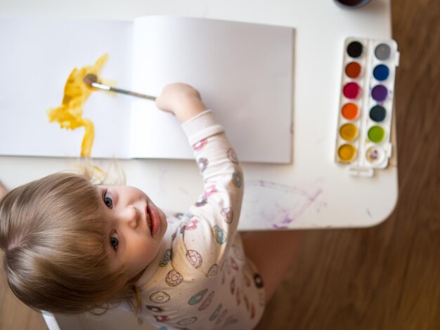 Een 2-jarig meisje zit aan een tafel en leert tekenen met veelkleurige aquarellen Kindercreativiteit Kinderhobby's