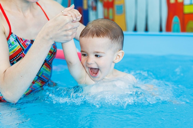 Een 2-jarige jongen leert zwemmen in een zwembad met een coach Zwemlessen voor kinderen Zwemschool voor kinderen Educatieve zwemcursussen voor kinderen