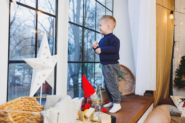 Een 2-jarige jongen zit op de vensterbank in het nieuwe jaar Nieuwjaars sfeer thuis Het kind wacht op het nieuwe jaar