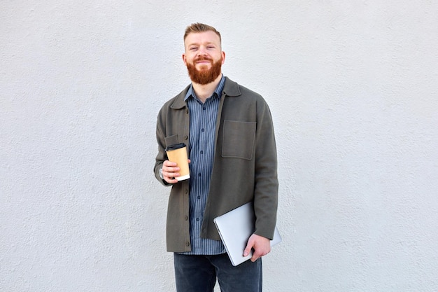 Foto een 35-jarige man met een rode baard loopt door de stad en drinkt koffie tijdens zijn lunchpauze op kantoor.