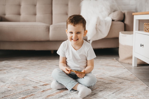 Een 5-jarige jongen kijkt naar een smartphone, het kind zit op de grond en houdt de telefoon vast