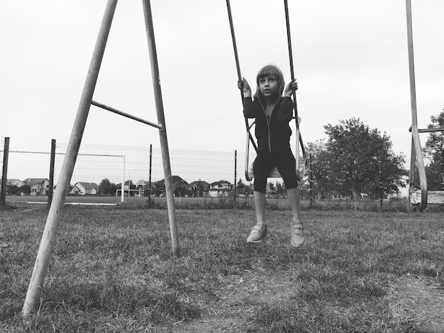 Een 67-jarig meisje zwaait op een schommel tegen de achtergrond van een voetbalveld Zwart-wit zwart-wit beeld in retro of vintage stijl Kaukasisch kind