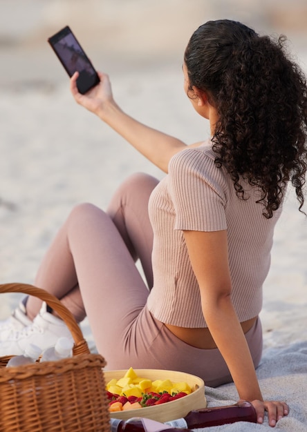 Een aantal van mijn favoriete momenten op het strand vastleggen. Shot van een onherkenbare vrouw die alleen op het strand zit en haar mobiel gebruikt om selfies te maken.