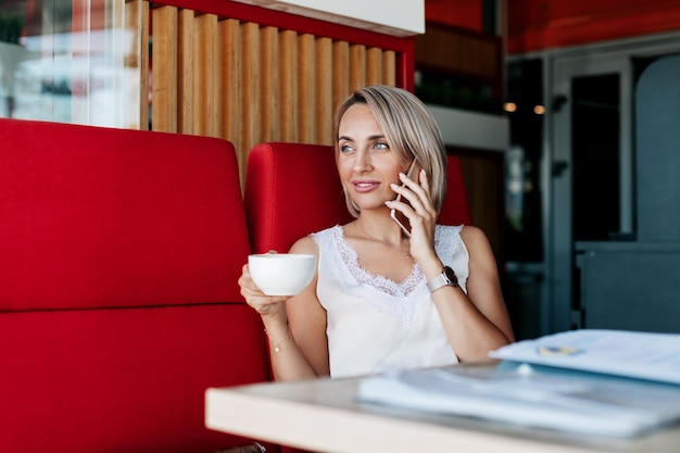 Foto een aantrekkelijk meisje praat op een mobiele telefoon en glimlacht terwijl ze alleen in een café zit