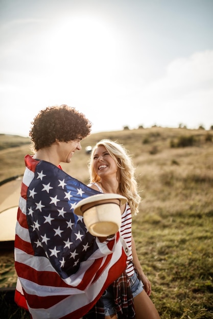 Een aantrekkelijk verliefd stel, gewikkeld in een Amerikaanse vlag, genietend van een tent op de camping.