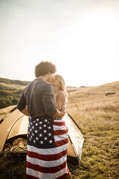 Een aantrekkelijk verliefd stel, gewikkeld in een Amerikaanse vlag, genietend van een tent op de camping.