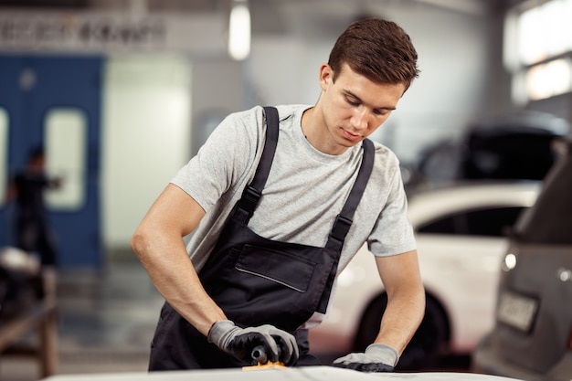 Een aantrekkelijke automonteur poetst op zijn werk een auto. Autoservice en onderhoud.