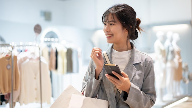 Een aantrekkelijke Aziatische vrouw met boodschappentassen geniet van winkelen in een winkelcentrum