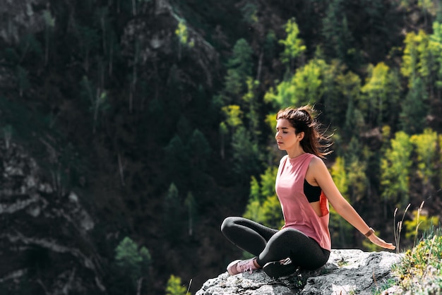 Een aantrekkelijke en gezonde jonge vrouw doet yoga in de bergen bij zonsopgang. Yoga in de frisse lucht. Gelukkige vrouw die yoga-oefeningen doet. Meditatie in de natuur. Een vrouw die yoga beoefent in de bergen