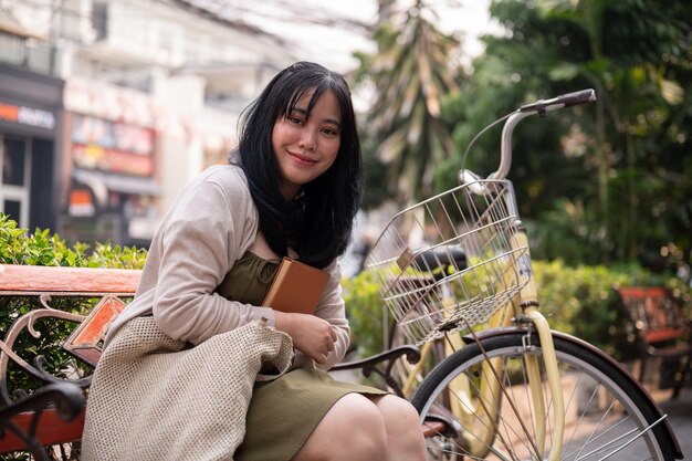 Een aantrekkelijke gelukkige jonge Aziatische vrouw zit op een bankje buiten in de stad met haar fiets