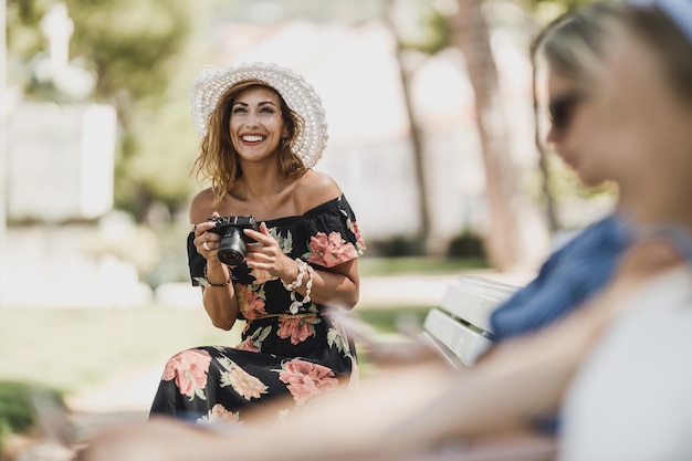 Een aantrekkelijke glimlachende vrouw die een digitale camera vasthoudt en geniet van tijd doorbrengen op een bankje in het park.