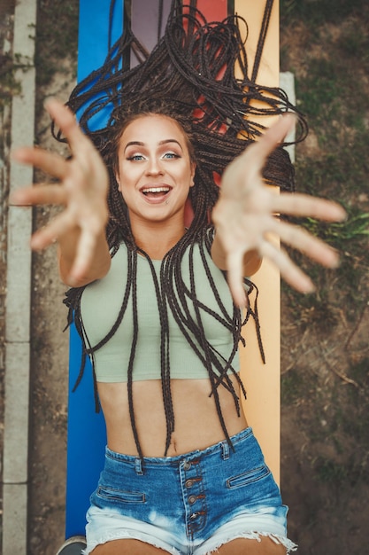 Een aantrekkelijke jonge blanke lachende vrouw met afro gevlochten haar ondergedompeld in gedachten ligt op de kleurrijke bank geniet in de zomerdag.