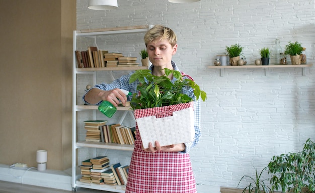 Een aantrekkelijke jonge man in een schort zorgt voor kamerplanten