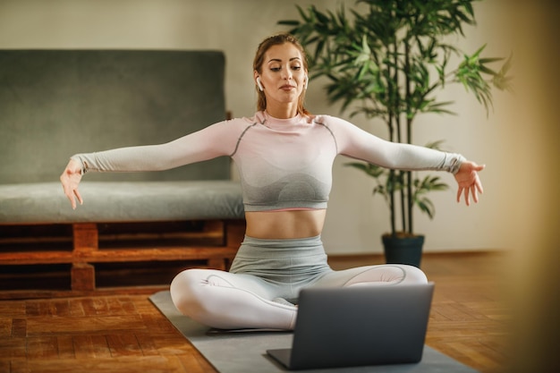 Een aantrekkelijke jonge vrouw die een laptop gebruikt om haar vlog over gezond leven op te nemen terwijl ze yoga beoefent in een studio.