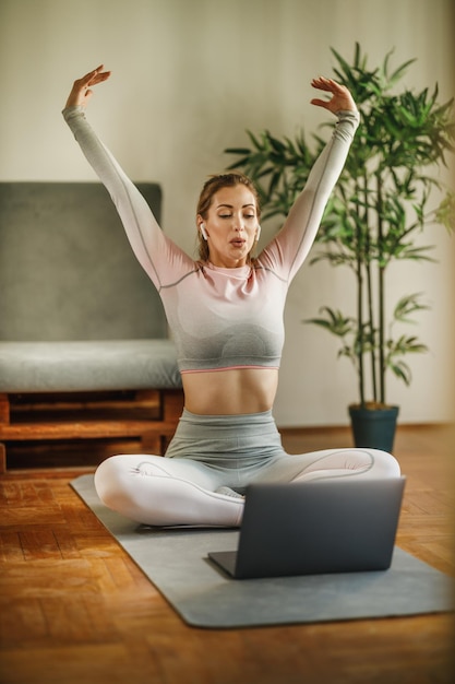 Een aantrekkelijke jonge vrouw die een laptop gebruikt om haar vlog over gezond leven op te nemen terwijl ze yoga beoefent in een studio.