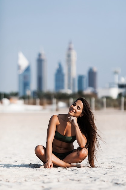 Een aantrekkelijke jonge vrouw die in bikini draagt, zit op een strand