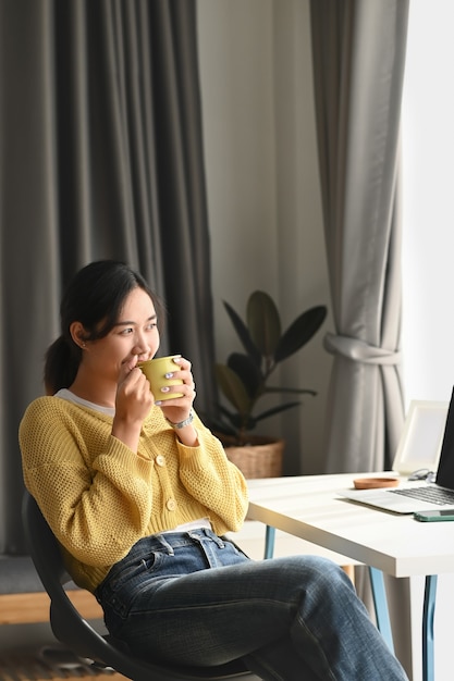 Een aantrekkelijke jonge vrouw drinkt koffie en ontspant zich op haar werkruimte