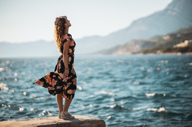 Een aantrekkelijke jonge vrouw in bloemenjurk die van een vakantie geniet terwijl ze een zomerdag aan de kust doorbrengt.