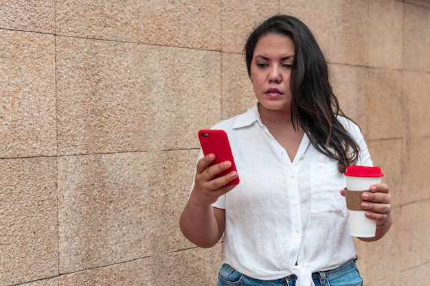 Een aantrekkelijke jonge vrouw in korte broek en blouse die haar mobiele telefoon op straat controleert.