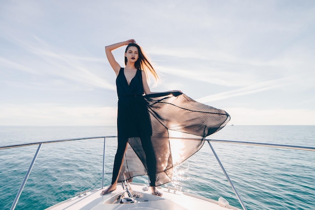 Een aantrekkelijke jonge vrouw in zwarte zomerkleren rust en ontspant op een jacht zeilen op de Caribische zee