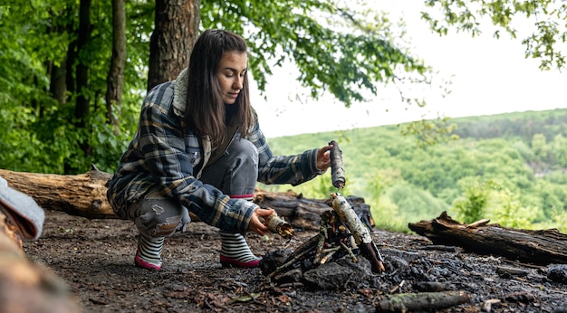 Een aantrekkelijke jonge vrouw maakt een vuur om warm te blijven in het bos