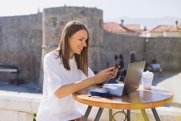 Een aantrekkelijke jonge vrouw met een mobiele telefoon in haar handen zit in een café Zomerdag en mooi weer