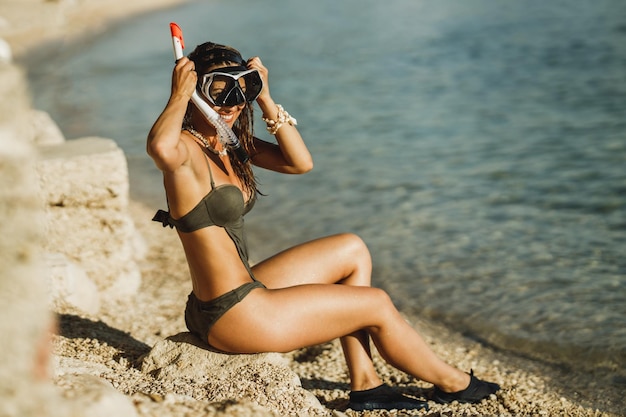 Een aantrekkelijke jonge vrouw zit aan het water met haar duikbril en snorkel en bereidt zich voor op snorkelen in de zee.