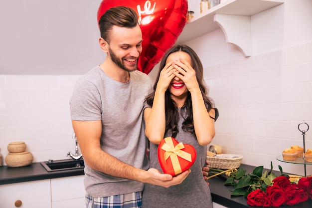 Een aantrekkelijke man en een knappe vrouw in huiskleding staan in de keuken en glimlachen terwijl ze elkaar cadeautjes geven op Valentijnsdag.