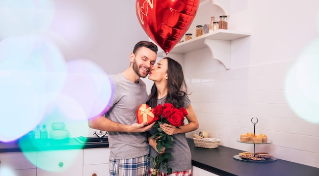 Een aantrekkelijke man en een knappe vrouw in huiskleding staan in de keuken en glimlachen terwijl ze elkaar cadeautjes geven op Valentijnsdag.