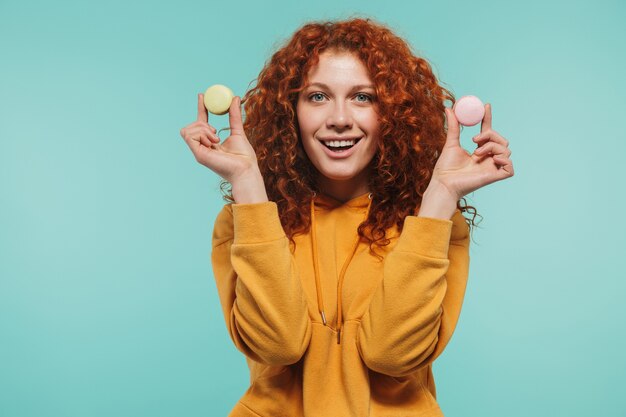 een aantrekkelijke roodharige jonge vrouw die geïsoleerd staat en bitterkoekjes toont