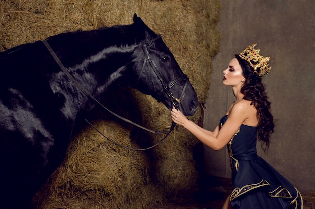 Een aantrekkelijke vrouw met een kroon die naar een zwart paard kijkt