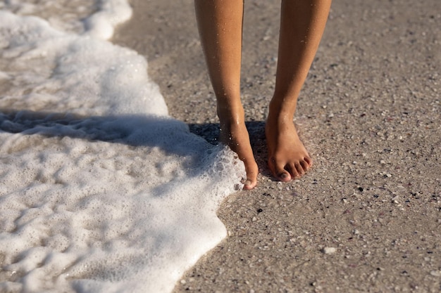 Een aantrekkelijke vrouw van gemengd ras die geniet van vrije tijd op het strand op een zonnige dag, staande op zand, een golf die haar blote voeten raakt. Ontspannende zomervakantie.