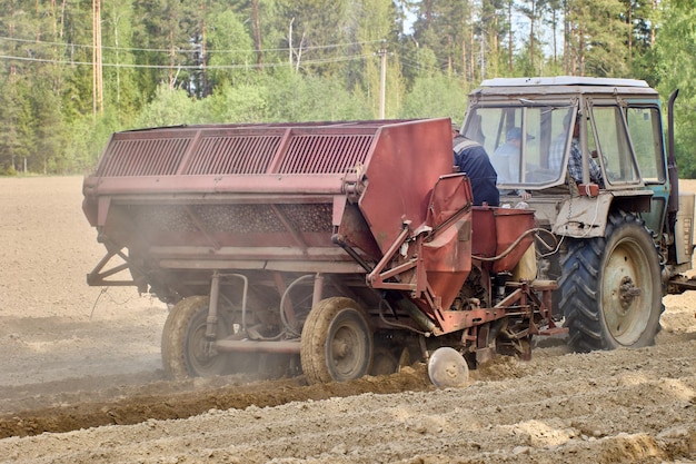 Een aardappelboer wordt tijdens het zaaien in het voorjaar aan een landbouwtraktor op wielen vastgemaakt.