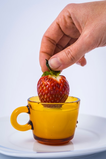 Een aardbei binnen een melkkop door een vrouwenhand op wit