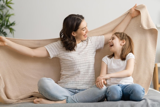 Een aardig meisje en haar moeder genieten van zonnige ochtend. Lekker thuis. Kind wordt wakker uit de slaap. Familie spelen onder deken op het bed in de slaapkamer.