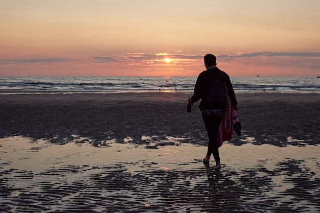 Een achteraanzicht van een dame die op het strand loopt en geniet van de schilderachtige zonsondergang